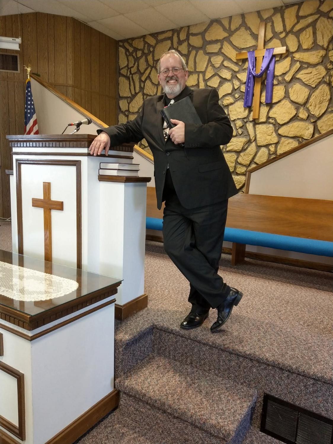 Pastor Rick Thompson standing by the pulpit with an open Bible.
