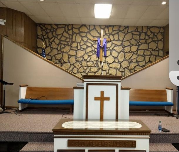 The sanctuary of Cornerstone Baptist Church, with the pulpit, wooden cross, and stone wall.